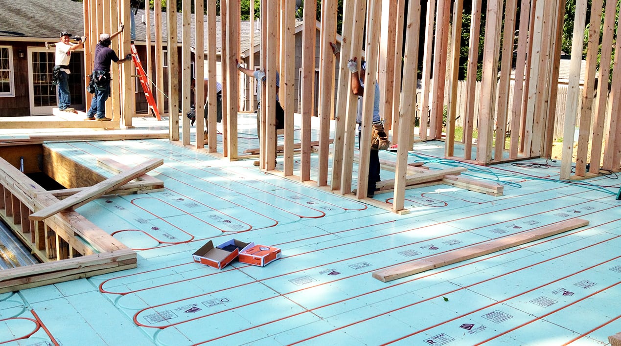 Workers lift framing over Warmboard-S with tubing already installed